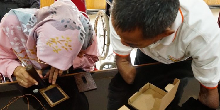 Penyandang disabilitas sedang membuat dompet cantik dari bahan pelepah pisang. (FOTO : ISTIMEWA)
